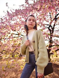 Portrait of beautiful young woman standing by flower tree