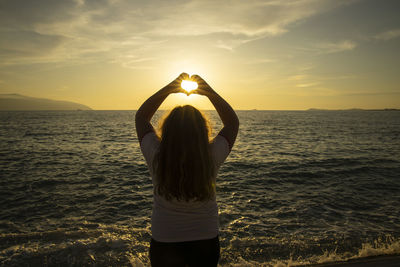 Rear view of woman standing by sea against sky during sunset