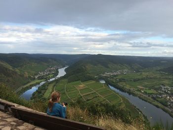 Rear view of girl sitting on mountain against cloudy sky