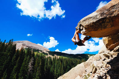 Low angle view of man climbing on mountain against blue sky