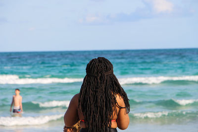 Rear view of woman standing at beach against sky