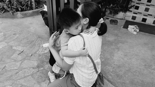 High angle view of mother embracing son while kneeling outdoors