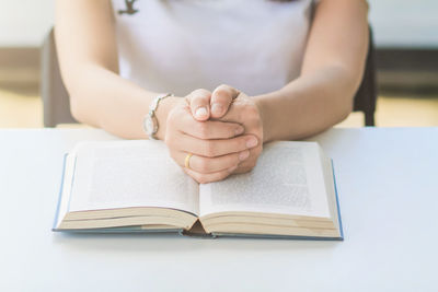 Midsection of woman with book sitting by table