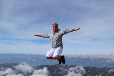 Full length portrait of man with arms outstretched jumping against sky