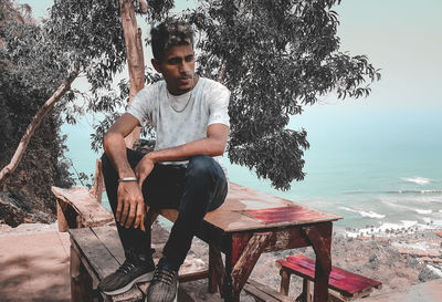 Young man sitting by plants against trees