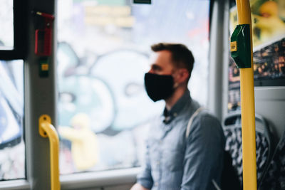 Close-up of mid adult man wearing mask sitting in bus