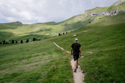 Rear view of man walking on grassland against sky