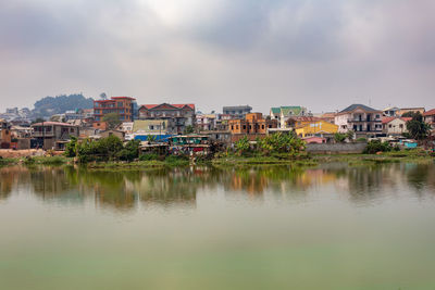 Scenic view of lake by buildings against cloudy sky