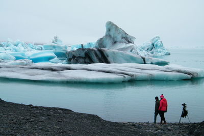 People standing on frozen lake against sky