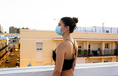 Young woman standing against building in city against clear sky