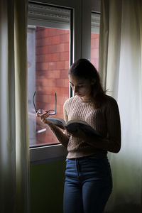 Young woman reading a book next to her window in the morning.