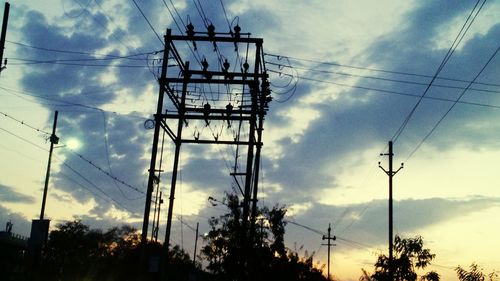 Low angle view of electricity pylon against cloudy sky