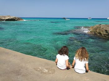 Rear view of female friends sitting by turquoise sea