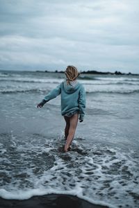 Rear view of woman standing at beach against sky