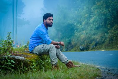 Full length of young man sitting by road