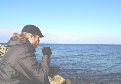 Side view of man drinking coffee on beach against sky