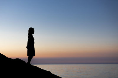 Side view of silhouette girl standing by sea during sunset
