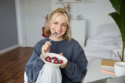 Portrait of smiling young woman eating food at home