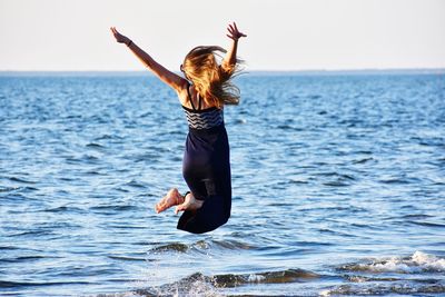 Rear view of woman jumping in sea against sky