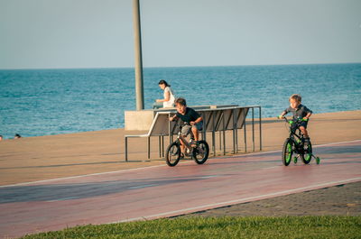 People sitting on bicycle by sea against sky