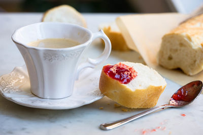 Close-up of coffee and baguette with strawberry jam on table