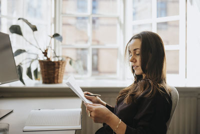 Side view of businesswoman examining document sitting at office