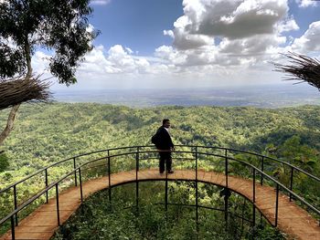 Rear view of man standing by railing against sky