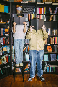 Male and female friends reading book while standing near shelf in bookstore