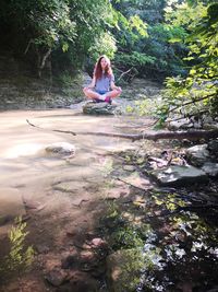 Young woman sitting by lake against trees