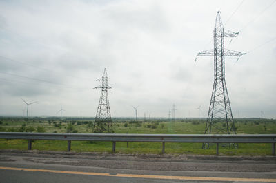 Electricity pylons on field against sky