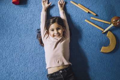 Portrait of happy girl lying on carpet with wooden toys in child care center