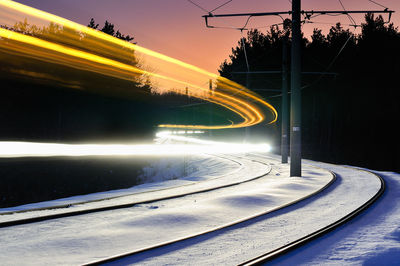 Light trails over railroad track covered with snow during sunset