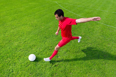 High angle view of man kicking soccer ball on field during sunny day