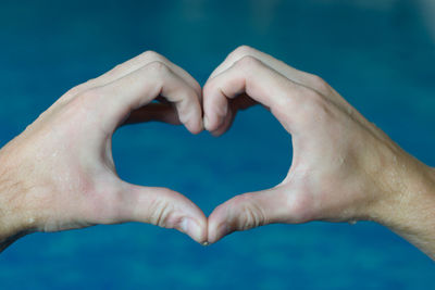 Cropped hands making heart shape against swimming pool