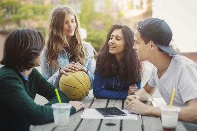 Male and female teenagers discussing at table outdoors