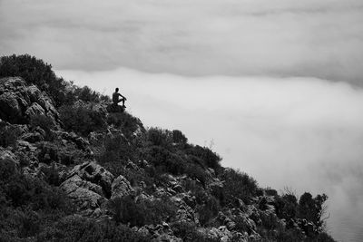 Man sitting on rock against sky