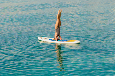 Full length of woman doing headstand on surfboard in sea