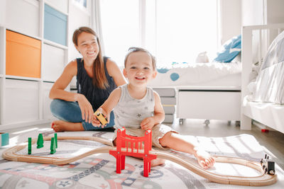 Mother and toddler boy playing with car wooden railway on floor at home. early age education 