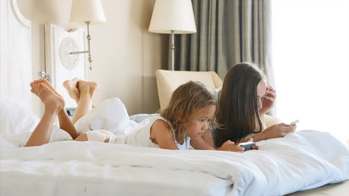 Mother and daughter using smart phone while relaxing on bed at home