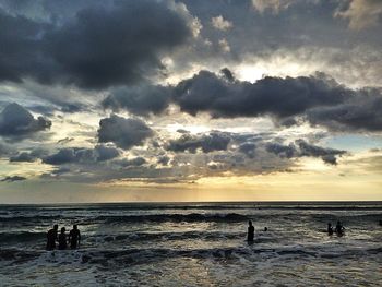 People on beach against cloudy sky