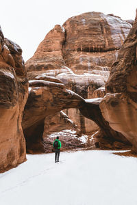 Rear view of hiker standing on snow amidst rock formation