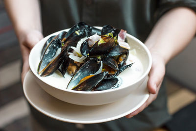 Midsection of person holding mussels in bowl