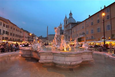 Fountain of neptune by old buildings against sky at dusk