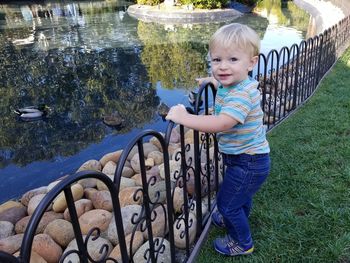 Portrait of cute boy showing ducks swimming on pond at park
