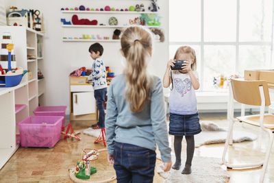 Little girl taking friend's photograph through toy camera at classroom