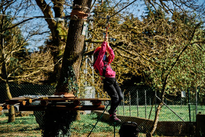 Little girl with protections practicing climbing between trees with ropes and nets