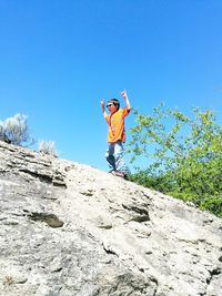 Low angle view of boy gesturing horn sign while standing on rock formation