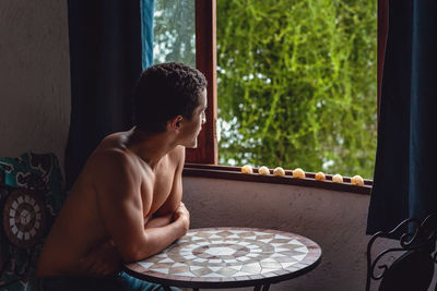 Young man looking through window at home
