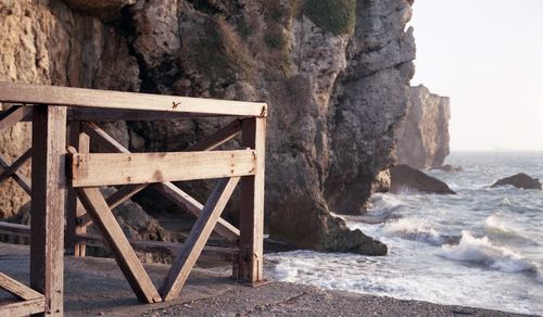 Wooden structure by rocks at sea shore against sky
