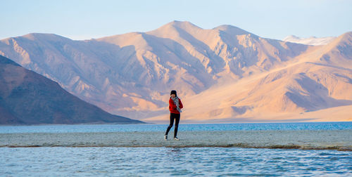 Full length of man standing in sea against mountains